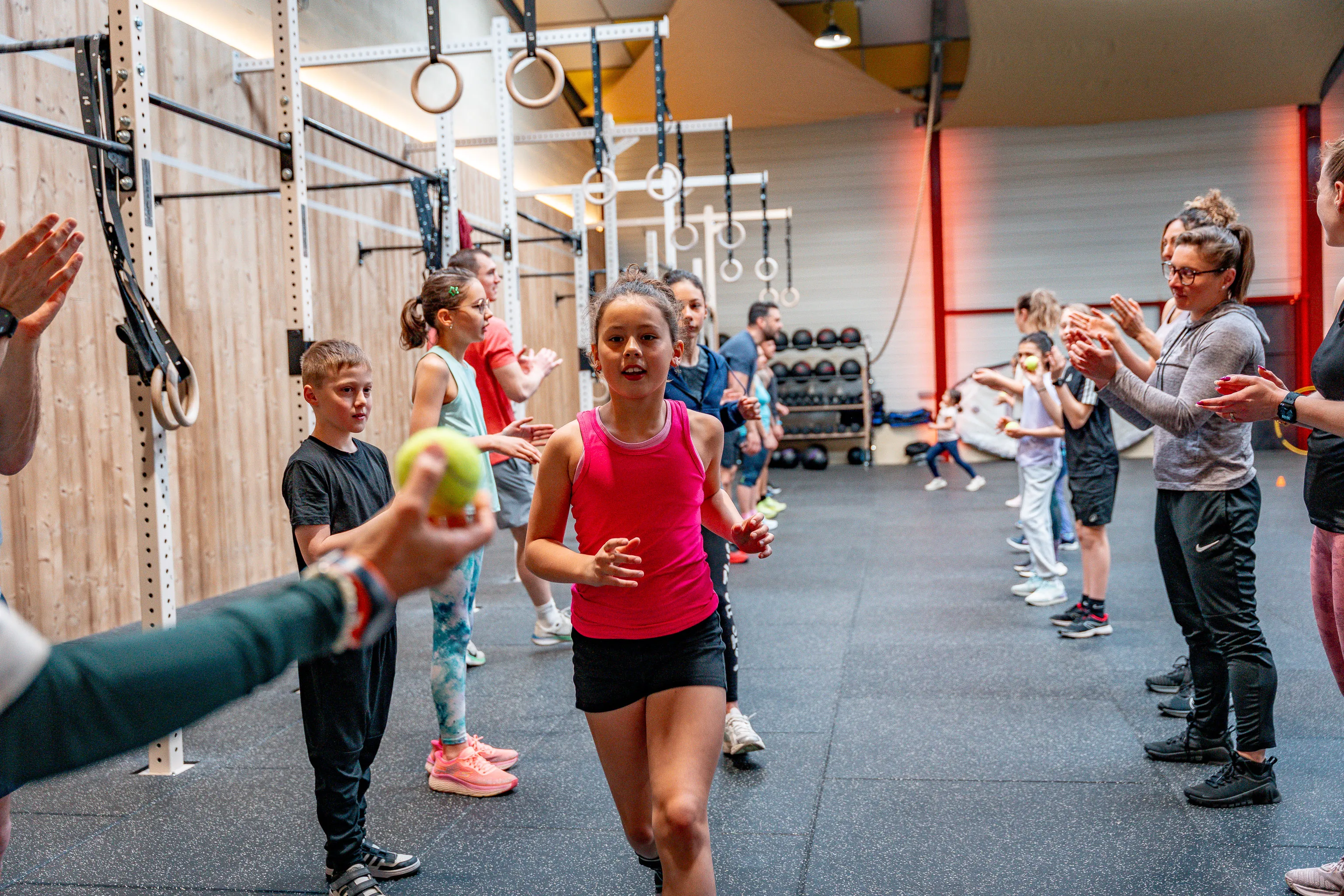 Une enfant court entre deux haies de camarades et de parents qui l'encouragent, pendant un cours CrossFit Kids au Côtière Sport Club