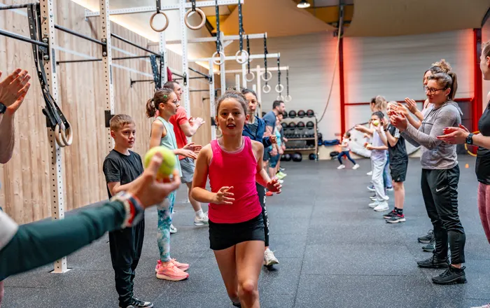 Une enfant court entre deux haies de camarades et de parents qui l'encouragent, pendant un cours CrossFit Kids au Côtière Sport Club